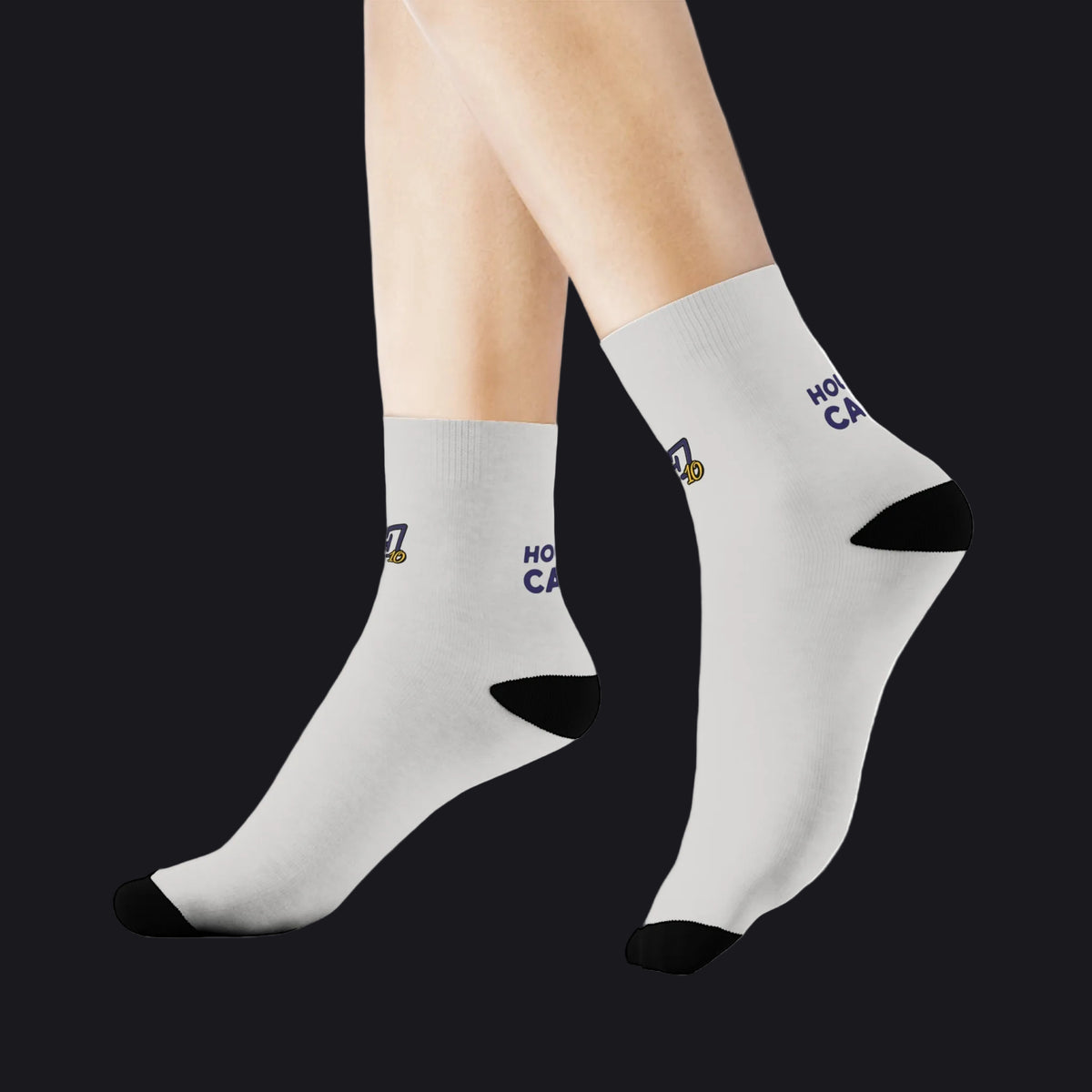 A pair of white crew socks with black toe and heel caps, featuring a small graphic and the text 'HONOR' and 'CA' on the side, shown on a model's feet against a white background.